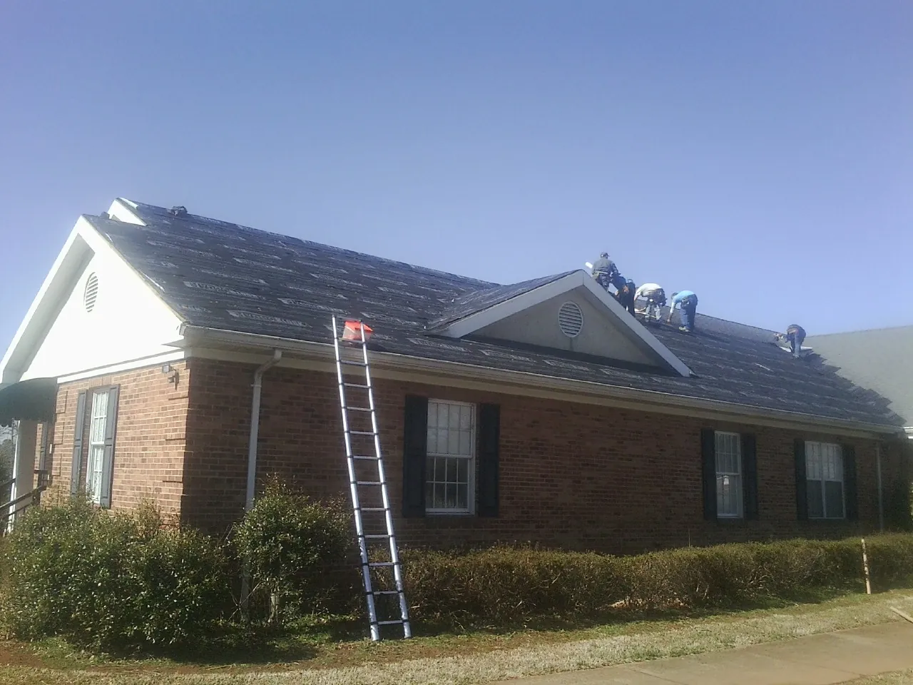 Crew tearing shingles off a brick ranch roof with a ladder set — Metal Roof Repair work by our crew in Oakhurst