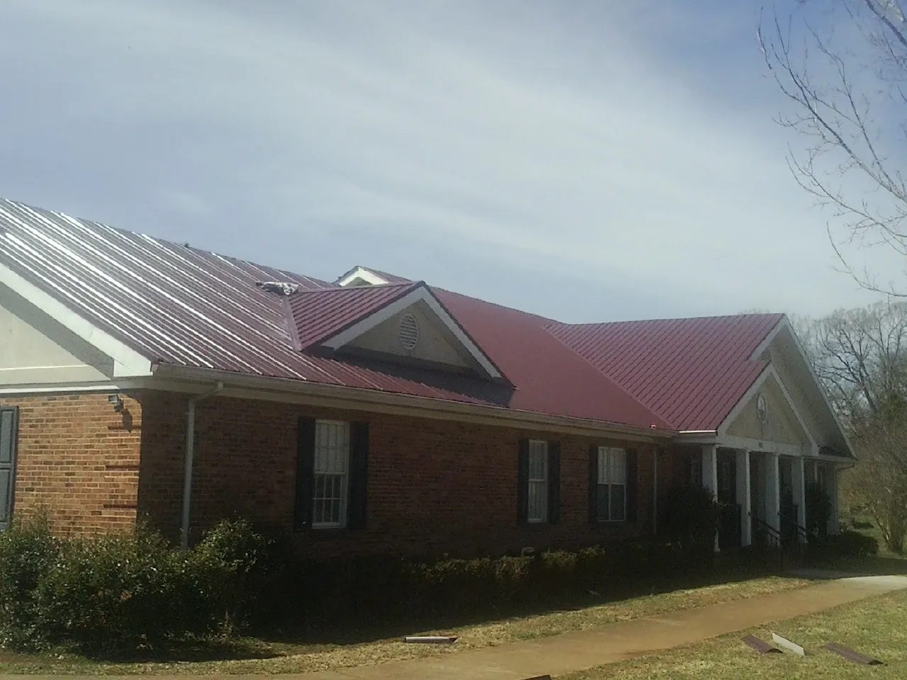 Red metal roof with gabled entries on a long brick building, from a Hail Damage Roof Repair job in Oakhurst