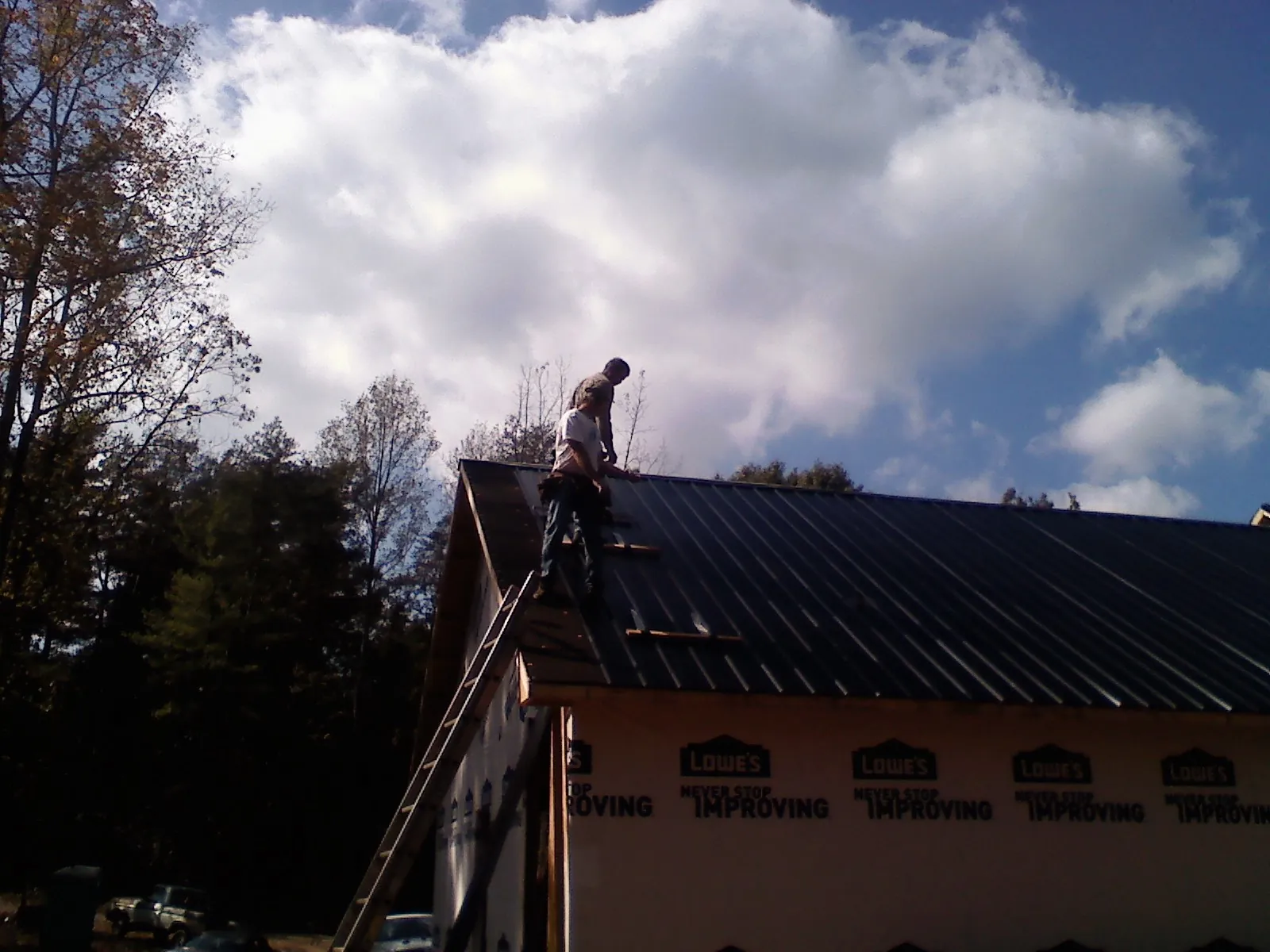 Roofer fastening dark metal panels high against a cloudy sky, from a Roof Inspection job in Oakhurst