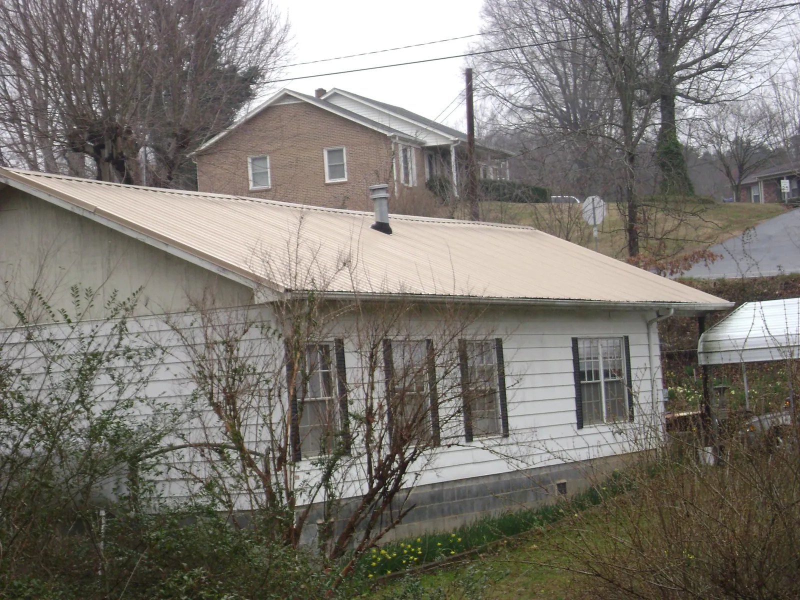 Tan metal roof on a white sided house set into a hillside — Commercial Roofing by Roofing Brothers in Oakhurst