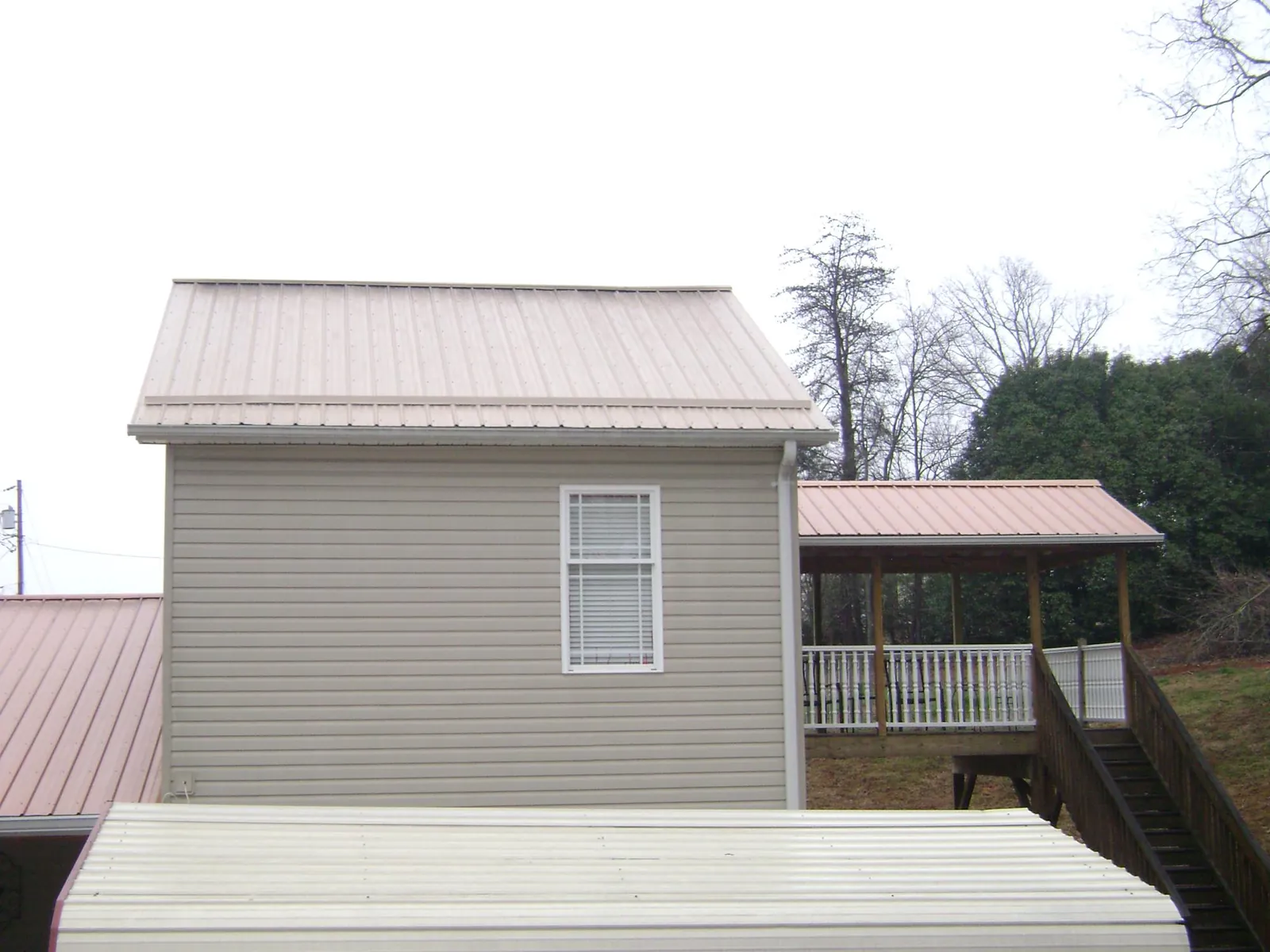 Tan metal roofs on a two story addition and attached porch, from a Roof Replacement job in Oakhurst